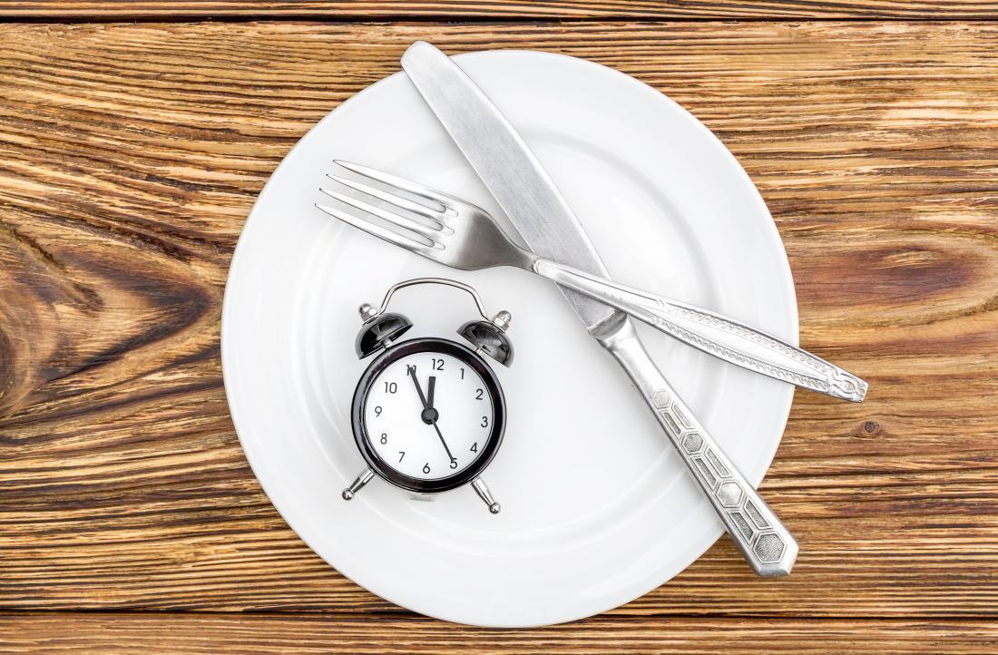 Pinggan kosong dengan pisau, garpu dan jam loceng di atas meja kayu.